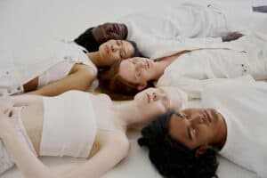 A diverse group of individuals lying down in a circle, all wearing white clothing, conveying unity.