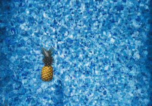 Vibrant pineapple floating in a blue mosaic tile pool, capturing summer vibes and tropical aesthetics.
